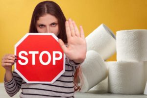 Dona con in mano uno stop, sullo sfondo diversi rotoli di carta igienica